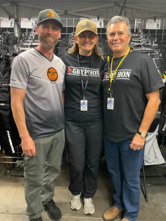 2 men standing on either side of a woman smiling wearing gryphon tshirts at a motorcycle show
