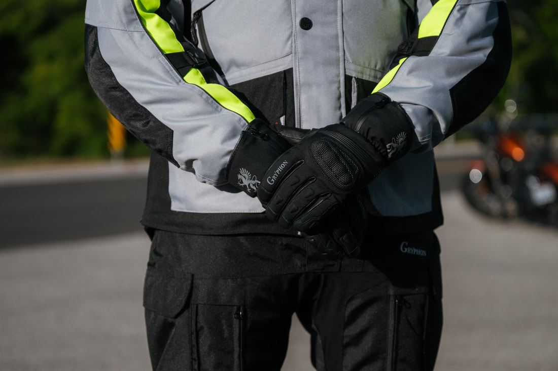 close up picture of man standing in a road with a motorcycle in the back wearing gryphon motorcycle pants and gryphon motorcycle jacket and gryphon motorcycle gloves