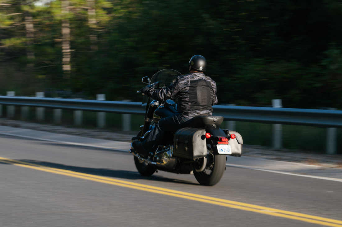 man riding away on a motorcycle on a highway wearing a gryphon motorcycle jacket and helmet