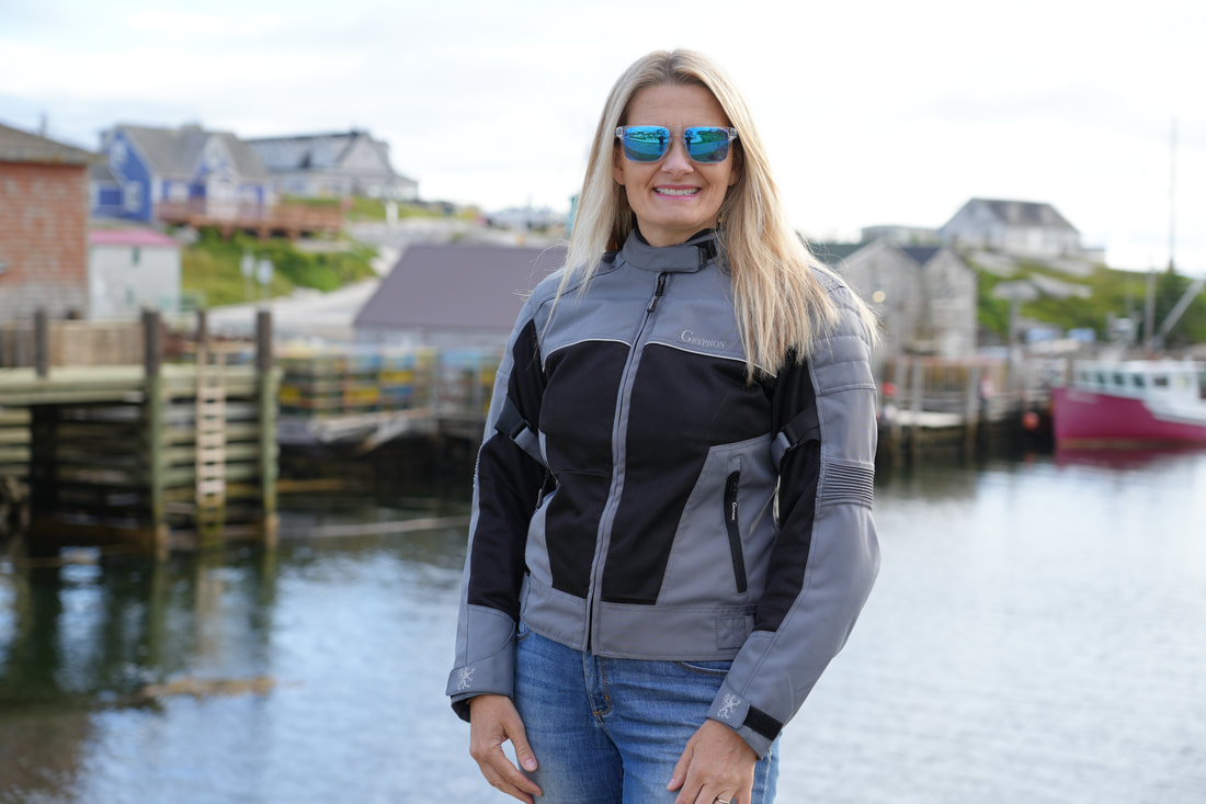 woman standing at a pier wearing a gryphon motorcycle jacket and sunglasses smiling