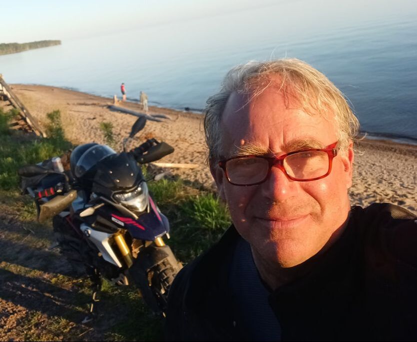man standing at the beach with his motorcycle behind