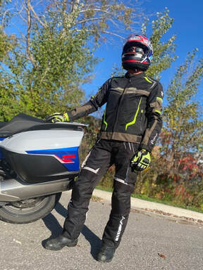 a man standing beside his motorcycle wearing gryphon protective motorcycle jacket, pants and gloves on a sunny day 