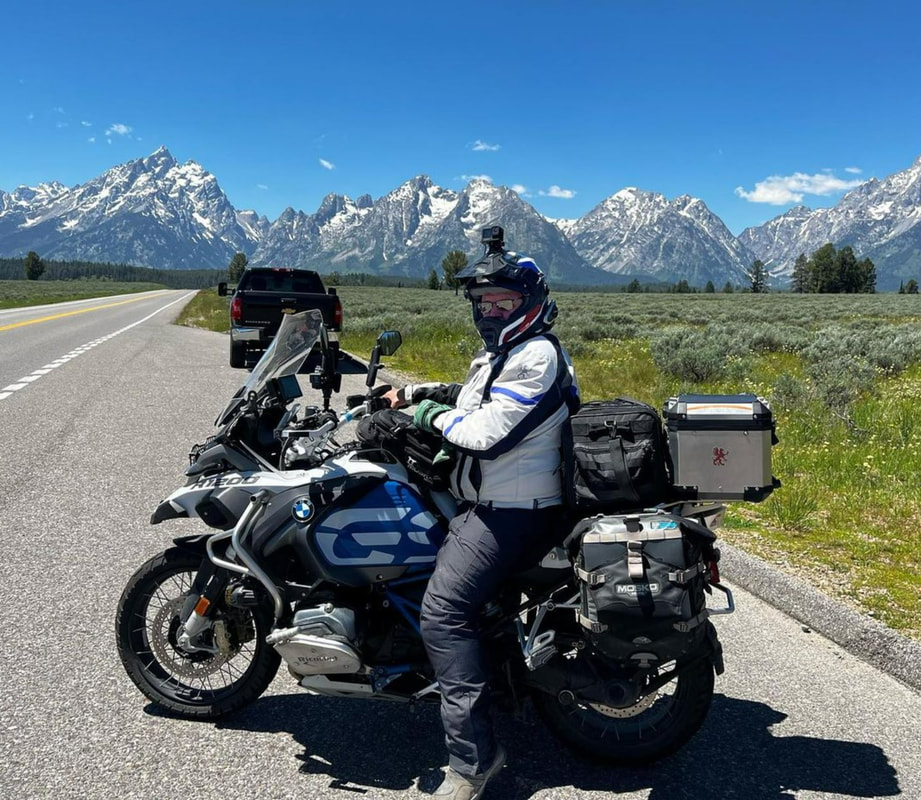 a man sitting on his motorcycle wearing gryphon protective motorcycle gear with a meadow and mountains in the background 
