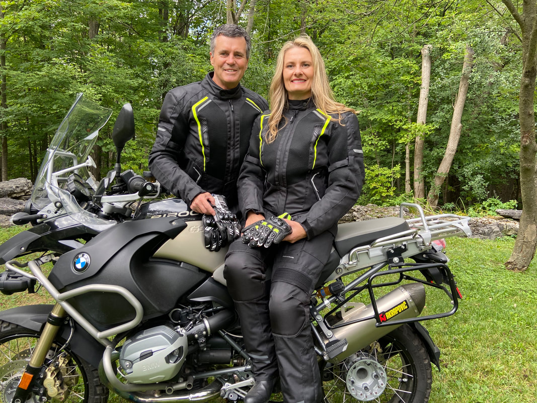 Woman sitting on a BMW motorcycle with a man standing behind wearing Gryphon motorcycle clothing