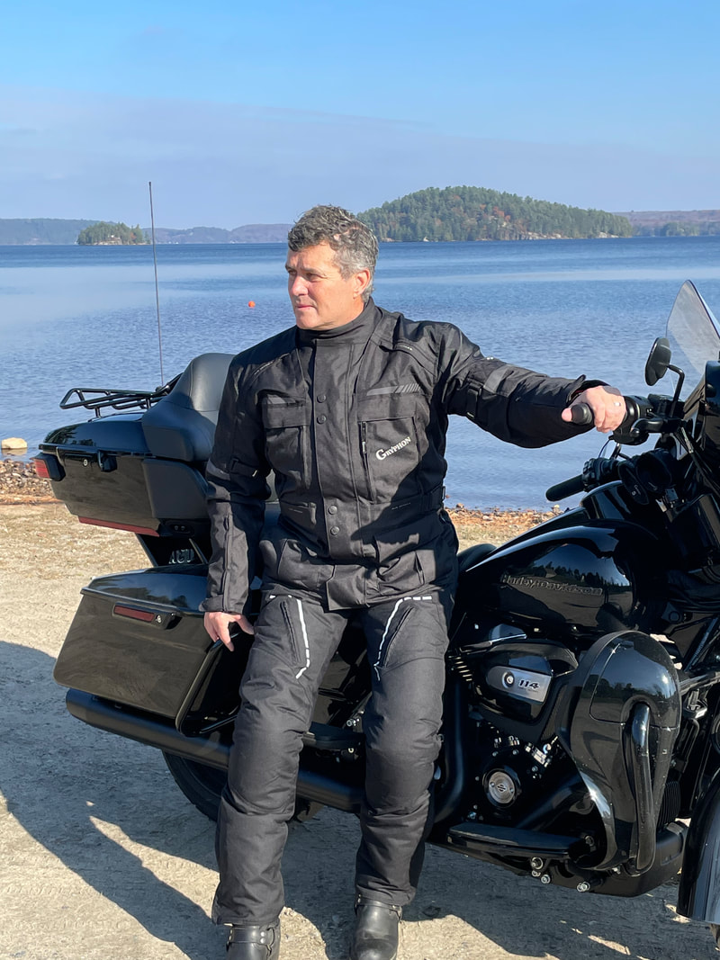 man sitting on a harley motorcycle at the beach looking away wearing a gryphon motorcycle jacket and gryphon motorcycle pants