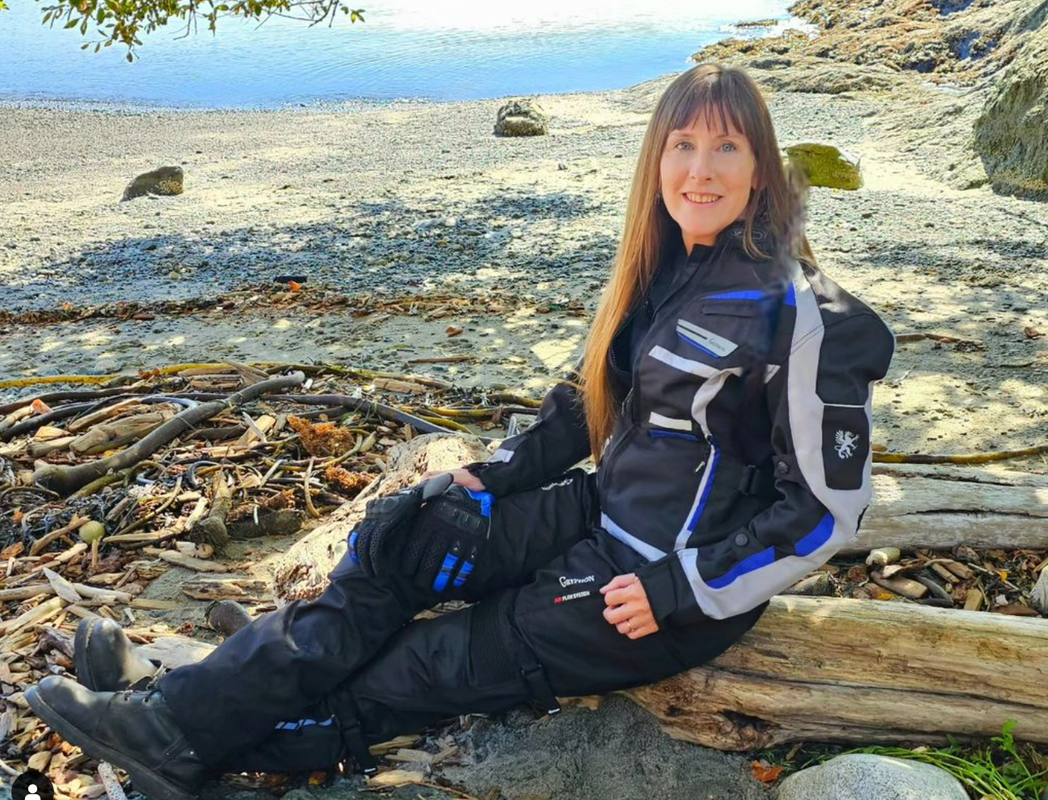 woman sitting on a log at the beach wearing gryphon motorcycle gear